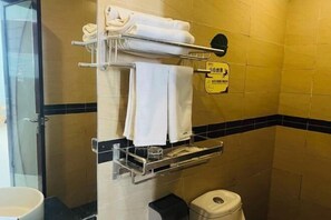 Een badkamer met een handdoekhouder, een prullenbak en een bord aan de muur.