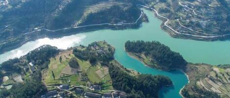 An aerial view of a terraced landscape with a river, terraced fields, and a cluster of buildings.