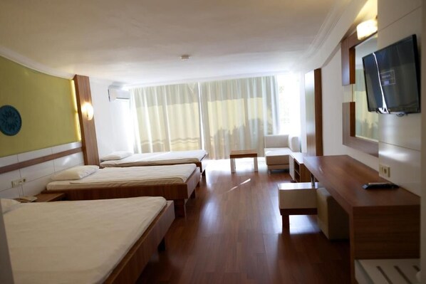 A hotel room with three beds, a desk, a chair, a TV, and a large window with curtains. - Club Golf Hotel - All Inclusive (Manavgat)