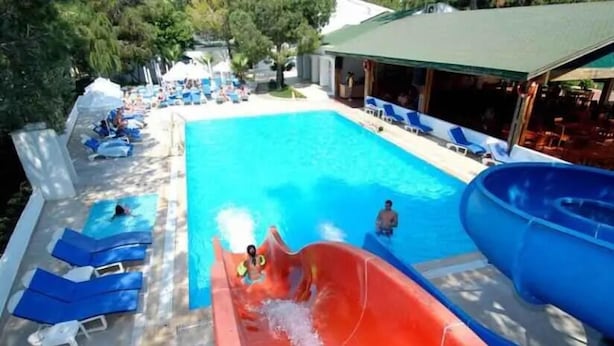 A swimming pool with a water slide, lounge chairs, and a covered area with tables and umbrellas. - Club Golf Hotel - All Inclusive (Manavgat)
