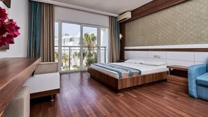 A modern hotel room with a wooden floor, a bed with a blue and white bedspread, a blue sofa, a desk with a chair, and a large window with curtains. - Club Golf Hotel - All Inclusive (Manavgat)