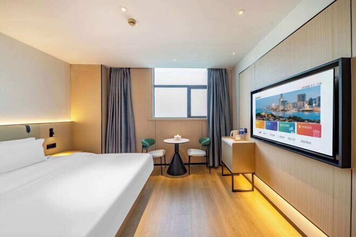 Een hotelkamer met een bed, een bureau, een stoel, een klein tafeltje, een televisie en een raam.