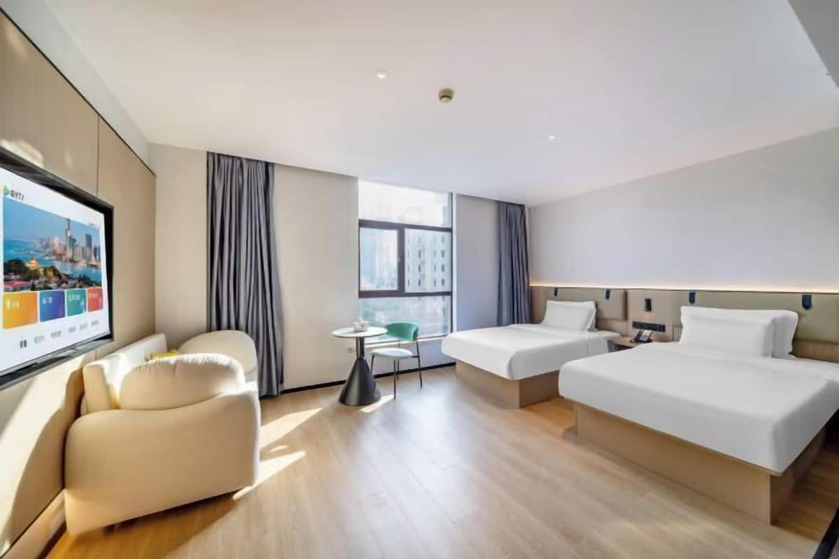 Hotelkamer met twee bedden, een bank, een kleine tafel en een televisiescherm waarop een stadsgezicht te zien is.