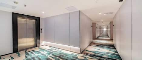 Un pasillo de hotel con piso alfombrado, un elevador empotrado en la pared y un largo corredor.