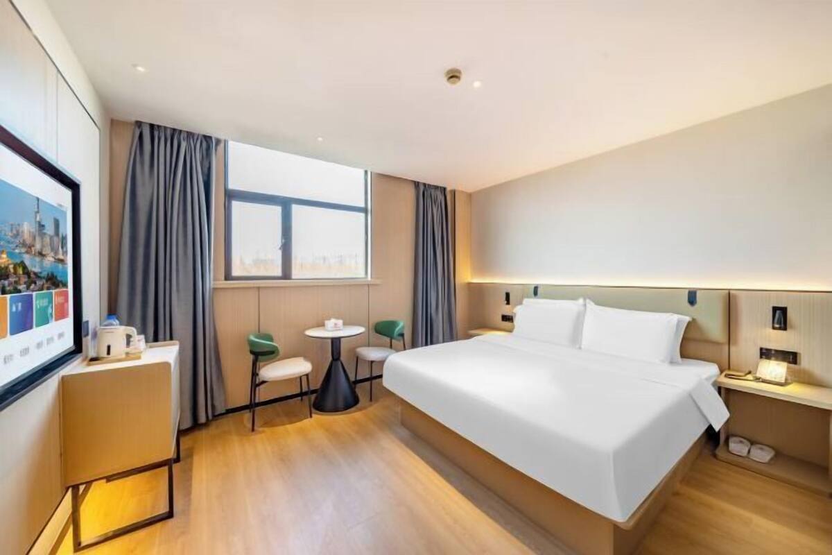 Een hotelkamer met een groot bed, een bureau, twee stoelen, een klein tafeltje en een raam met gordijnen.