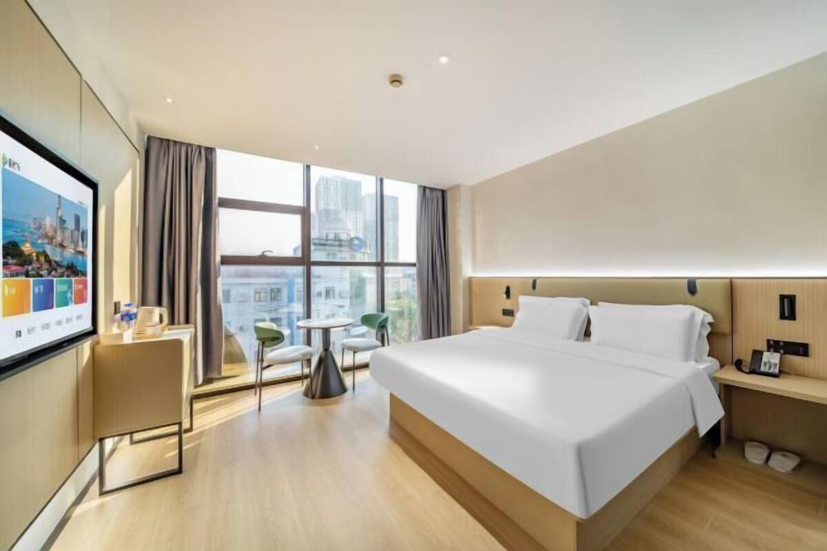 Een moderne hotelkamer met een groot bed, een bureau, een stoel, een televisie en een raam met uitzicht op de stad.