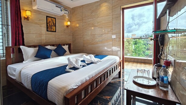 A hotel room with a bed, a TV, an air conditioning unit, a window with curtains, and a balcony with a table and chairs. - PV Tower - Auro Beach (Vanur)