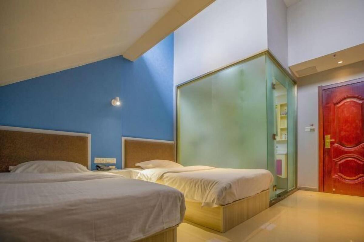 A hotel room with two beds, a red door, and a glass partition.