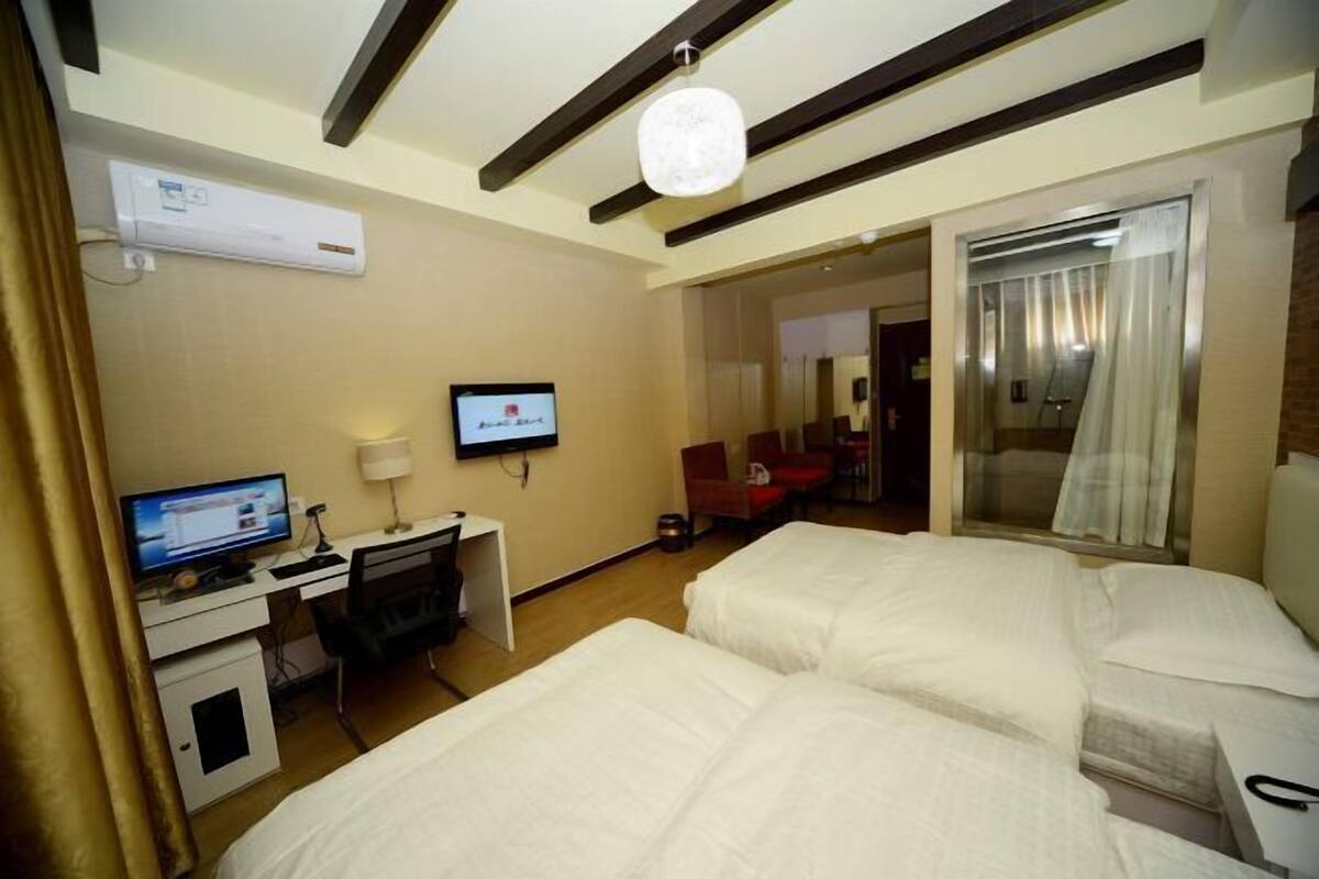 A hotel room with two beds, a desk with a computer, a TV, and an air conditioning unit.