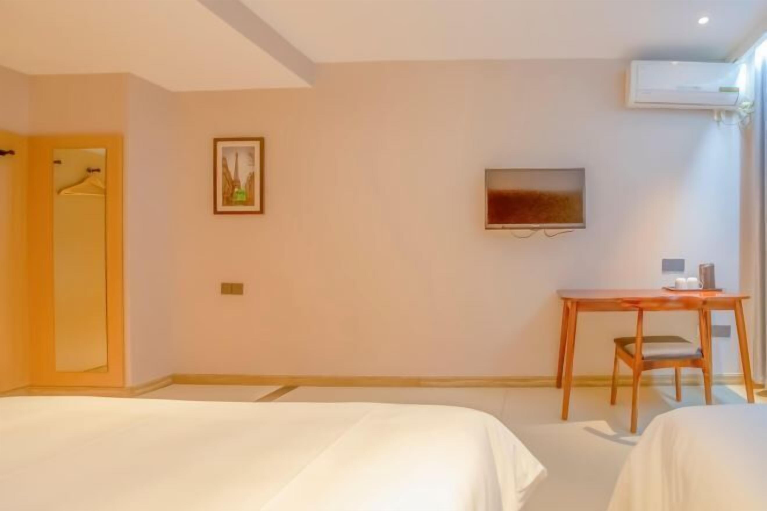 Een hotelkamer met twee bedden, een bureau, een stoel, een televisie en een airconditioning.