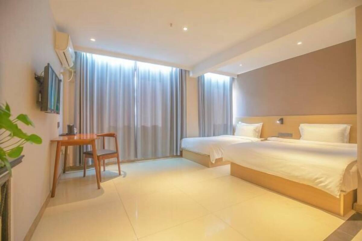 A hotel room with a bed, a desk, a chair, a TV, and a window with curtains.