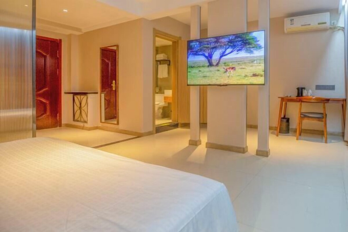 A hotel room with a bed, a TV mounted on the wall, a desk, and a chair.