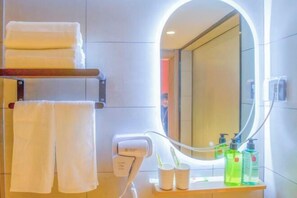A bathroom with a towel rack holding two towels, a hairdryer, and a mirror with a light. There are two bottles of liquid soap on the counter. - Home Inn Huayi Select Hotel (Yantai Zhaoyuan Fuqian Square) (Zhaoyuan)