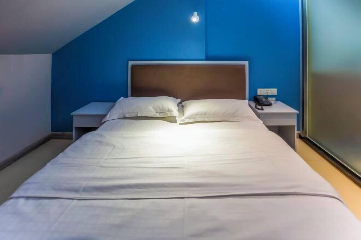 A single bed with white linens, a wooden headboard, a bedside table with a phone, and a wall-mounted light.
