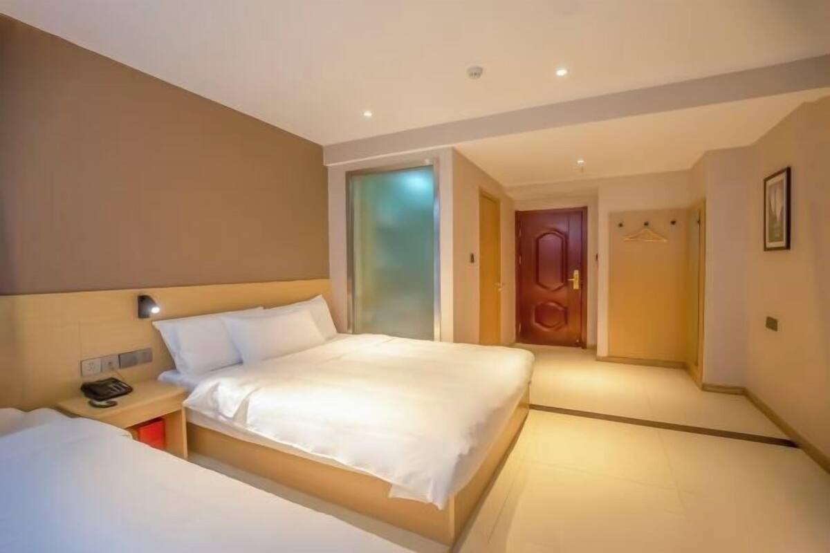A hotel room with a large bed, bedside table with a phone, and a door leading to another room.