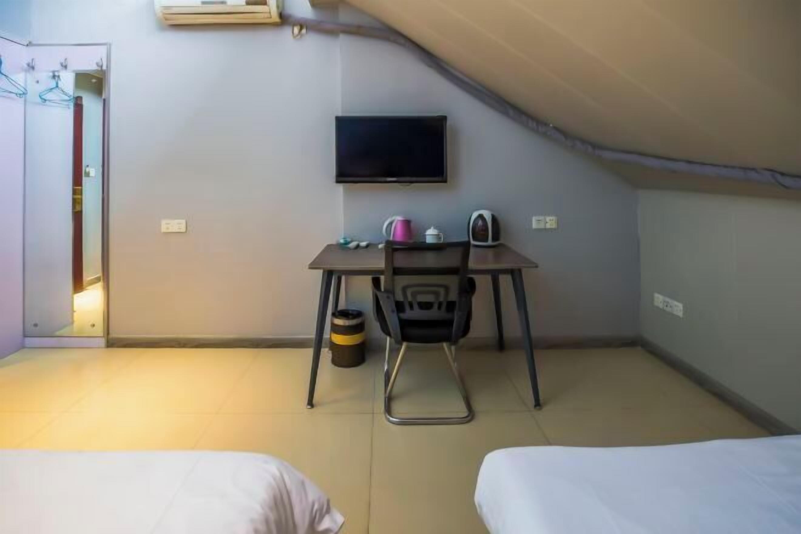 A small room with two beds, a desk with a chair, a television, and a trash bin.