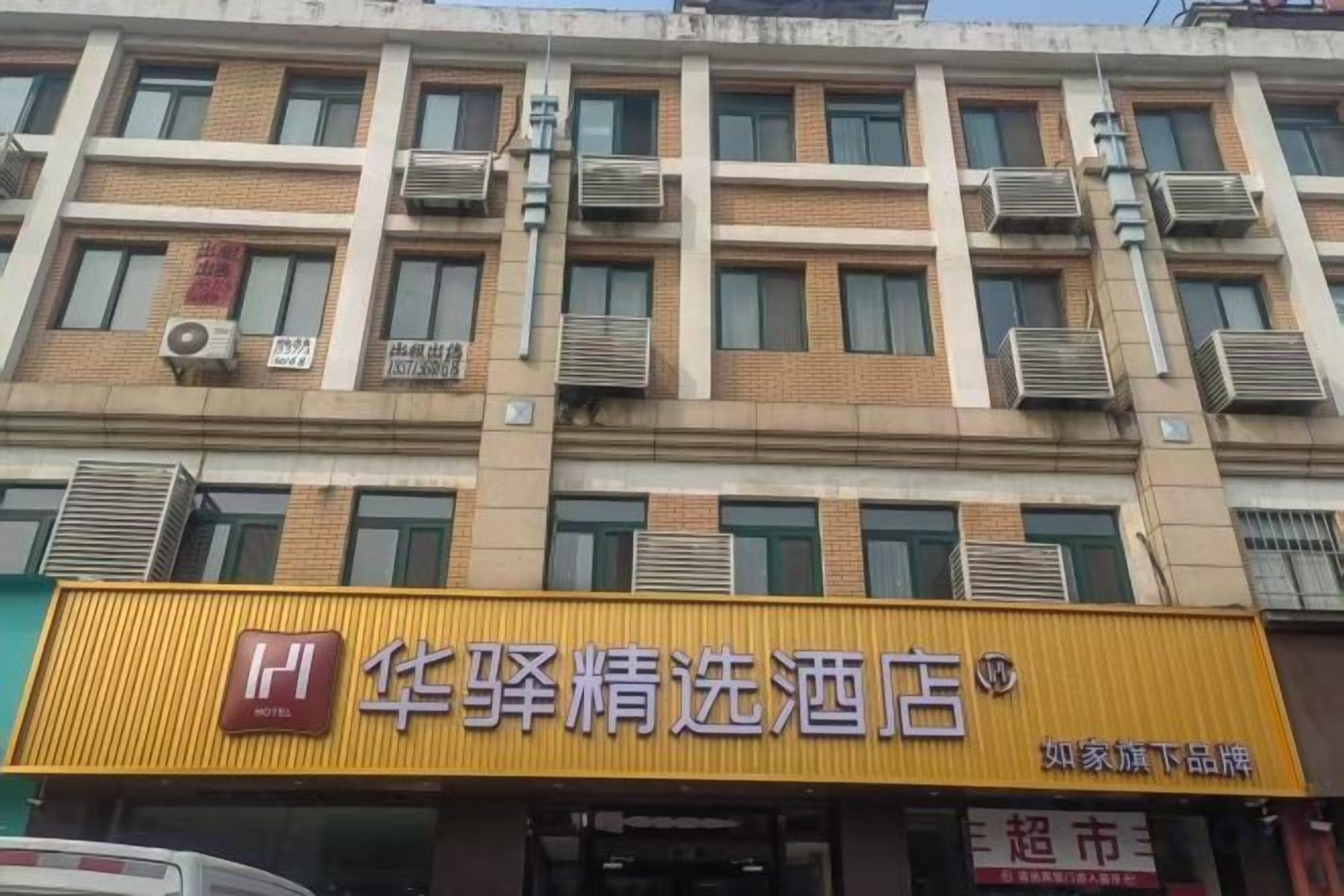 A hotel with multiple floors, air conditioning units on the exterior, and a prominent yellow sign with Chinese characters.