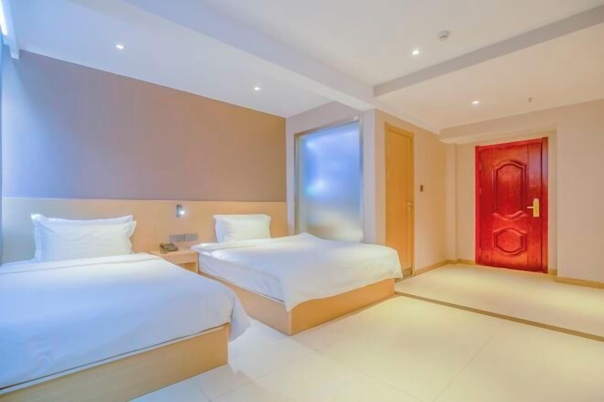 A hotel room with two beds, a red door, and a modern design.