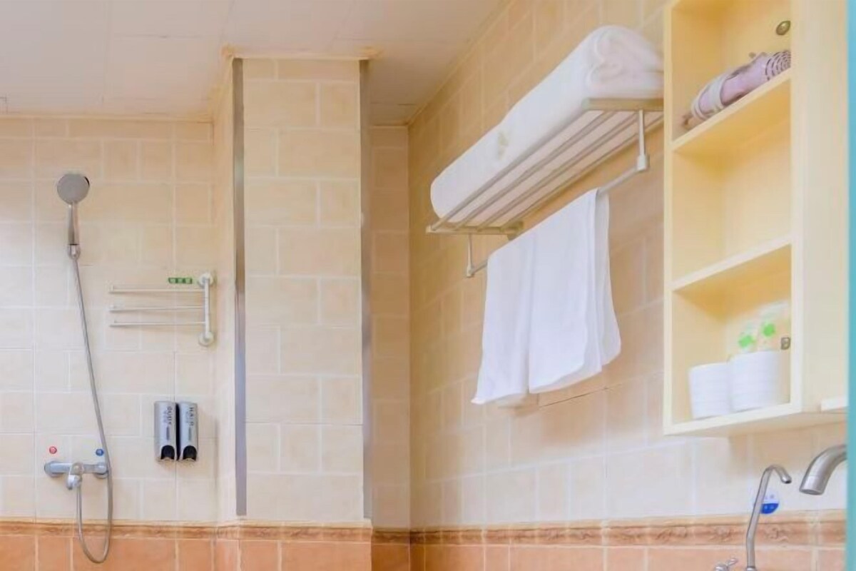 A bathroom with a shower, a towel rack, a shelf with toiletries, and a sink.