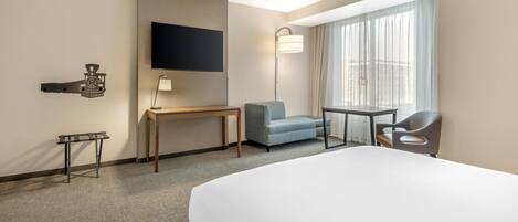 Hotelkamer met een groot bed, een bureau, een stoel, een aan de muur bevestigde televisie en een raam met gordijnen.