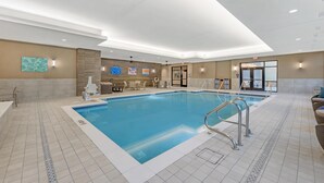 A large indoor swimming pool with a tiled floor, a pool ladder, and lounge chairs along the sides.