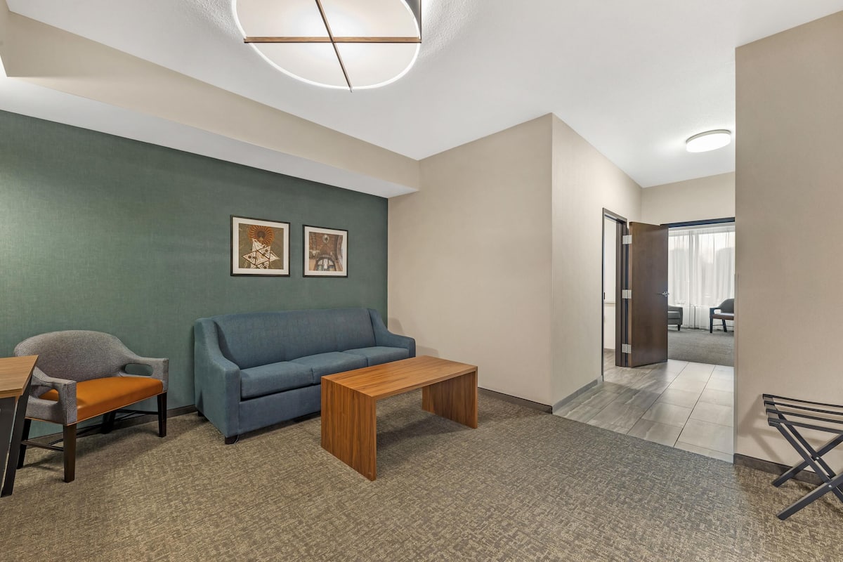 A modern office space with a blue sofa, wooden coffee table, and a chair. There are two framed pictures on the wall, a ceiling light fixture, and a door leading to another room.