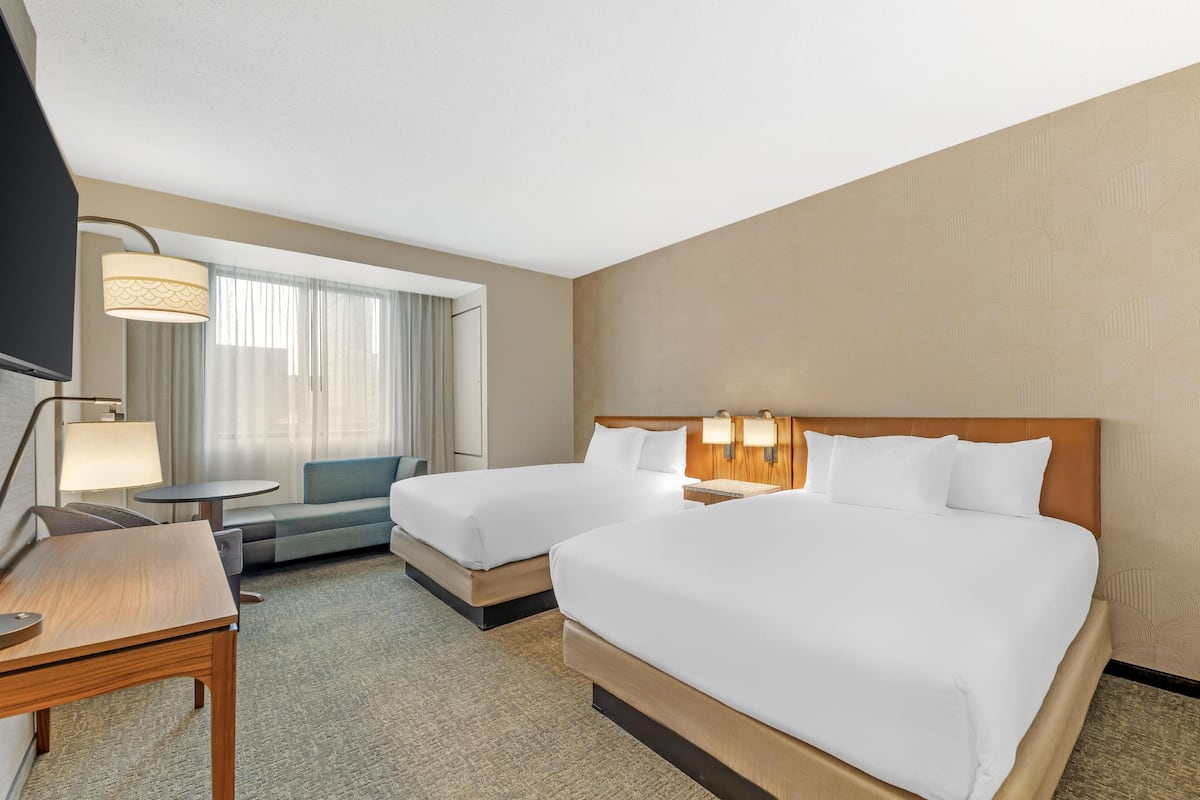 A hotel room with two beds, a sofa, a desk, and a TV.