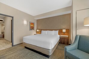 A hotel room with a large bed, a wooden headboard, a nightstand, a lamp, a blue armchair, and a poster on the wall. - Drury Plaza Hotel Lincoln Downtown (Lincoln)
