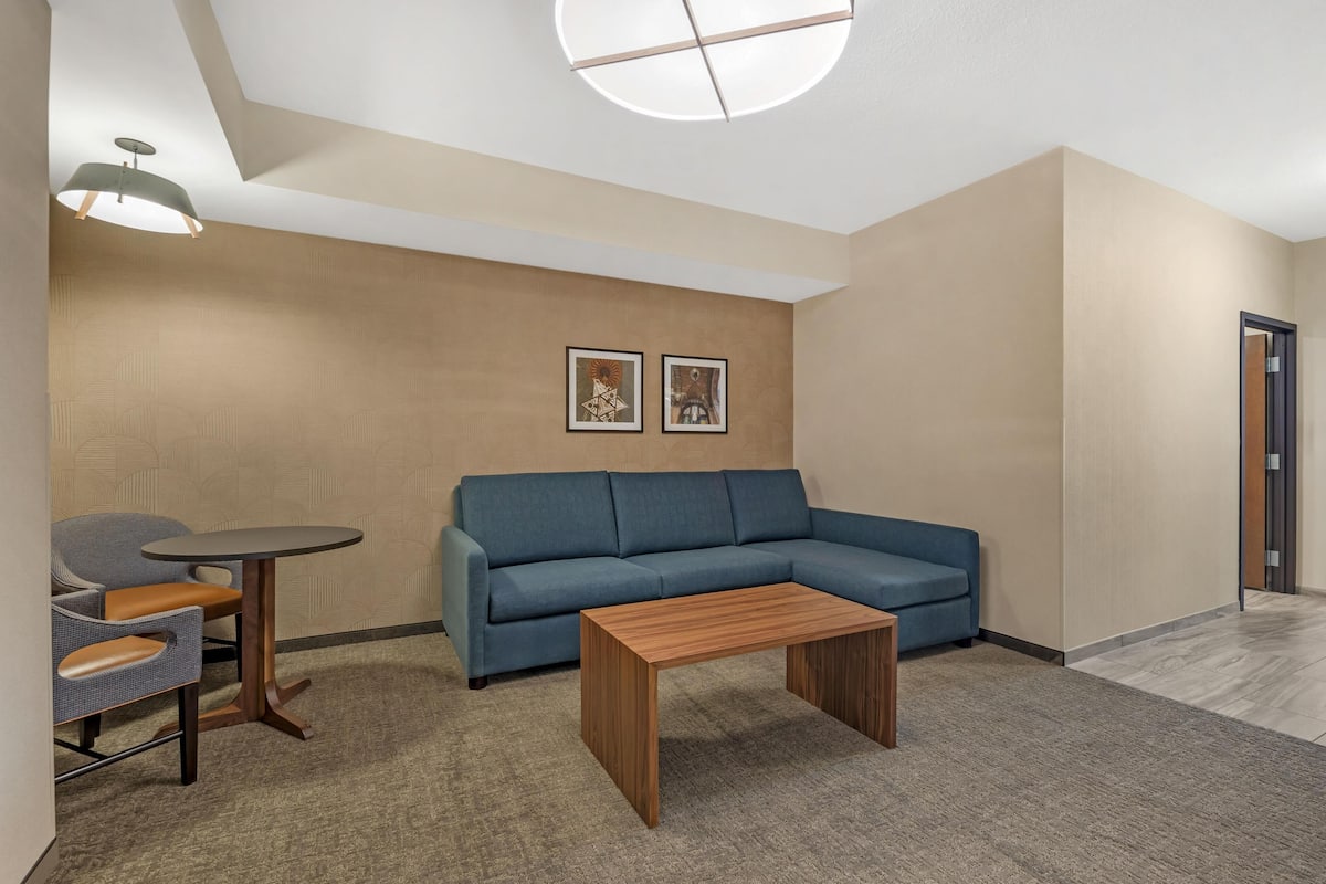 A modern room with a blue sofa, a small wooden table, and a round table with chairs. There are two framed pictures on the wall.