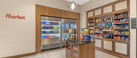 A grocery store interior with a refrigerated section, snack shelves, and a wooden counter.