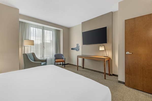 A hotel room with a large bed, a desk, a chair, a TV mounted on the wall, and a door. - Drury Plaza Hotel Lincoln Downtown (Lincoln)