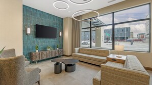 A modern hotel lobby with a large window, a flat-screen TV, and a seating area with sofas and tables.