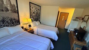 Ein Hotelzimmer mit zwei Betten, einem Schreibtisch, einem Stuhl, einer Lampe, einem Gemälde und einer Tür.