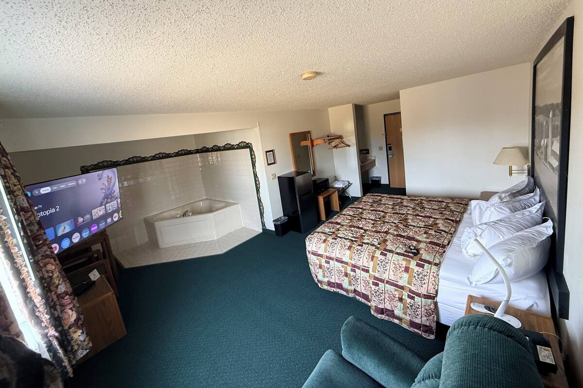 Et hotelværelse med seng, skrivebord, stol, fjernsyn, badekar og en dør.