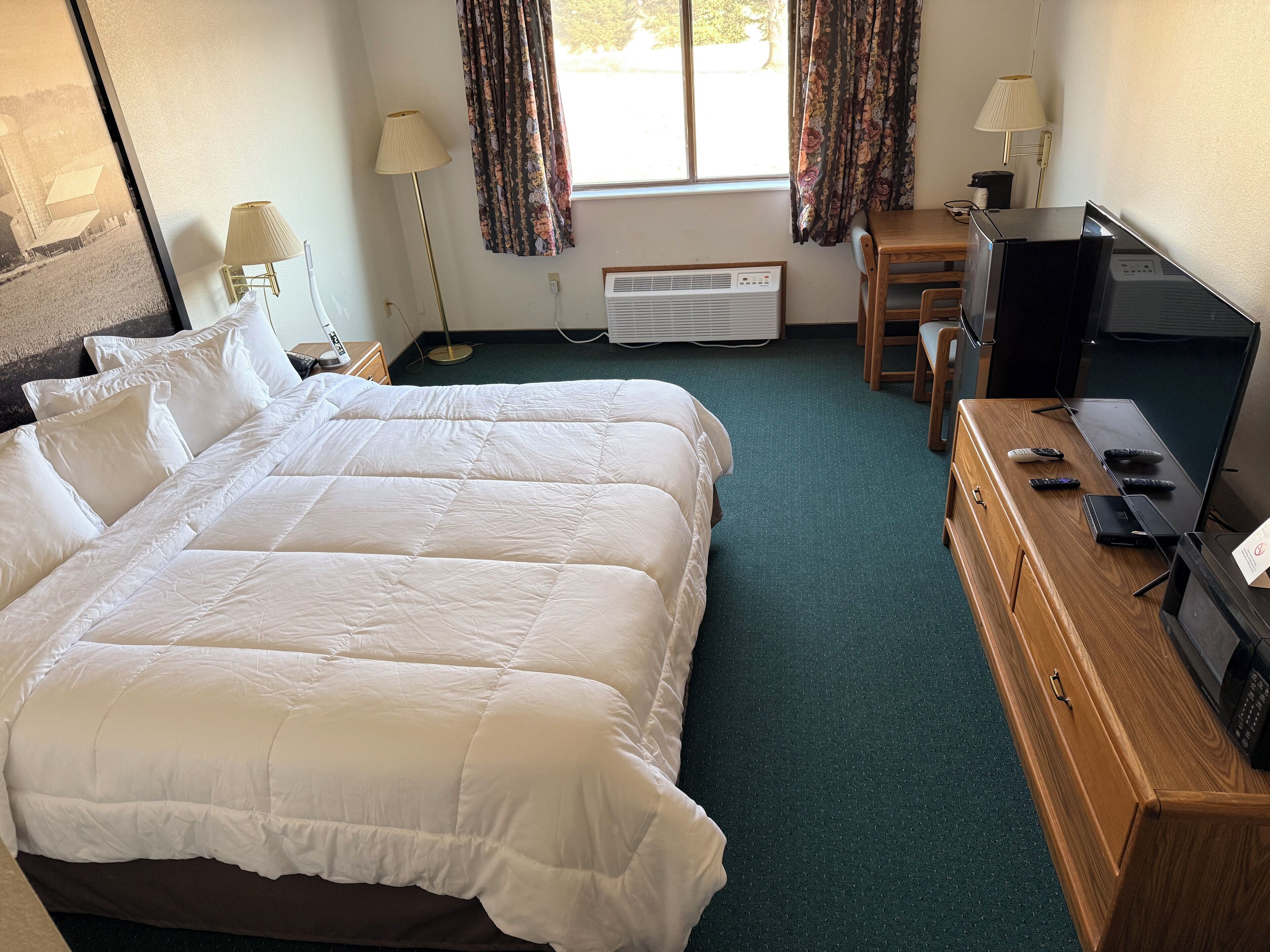 A hotel room with a large bed, a desk with a computer, a TV, and two lamps.