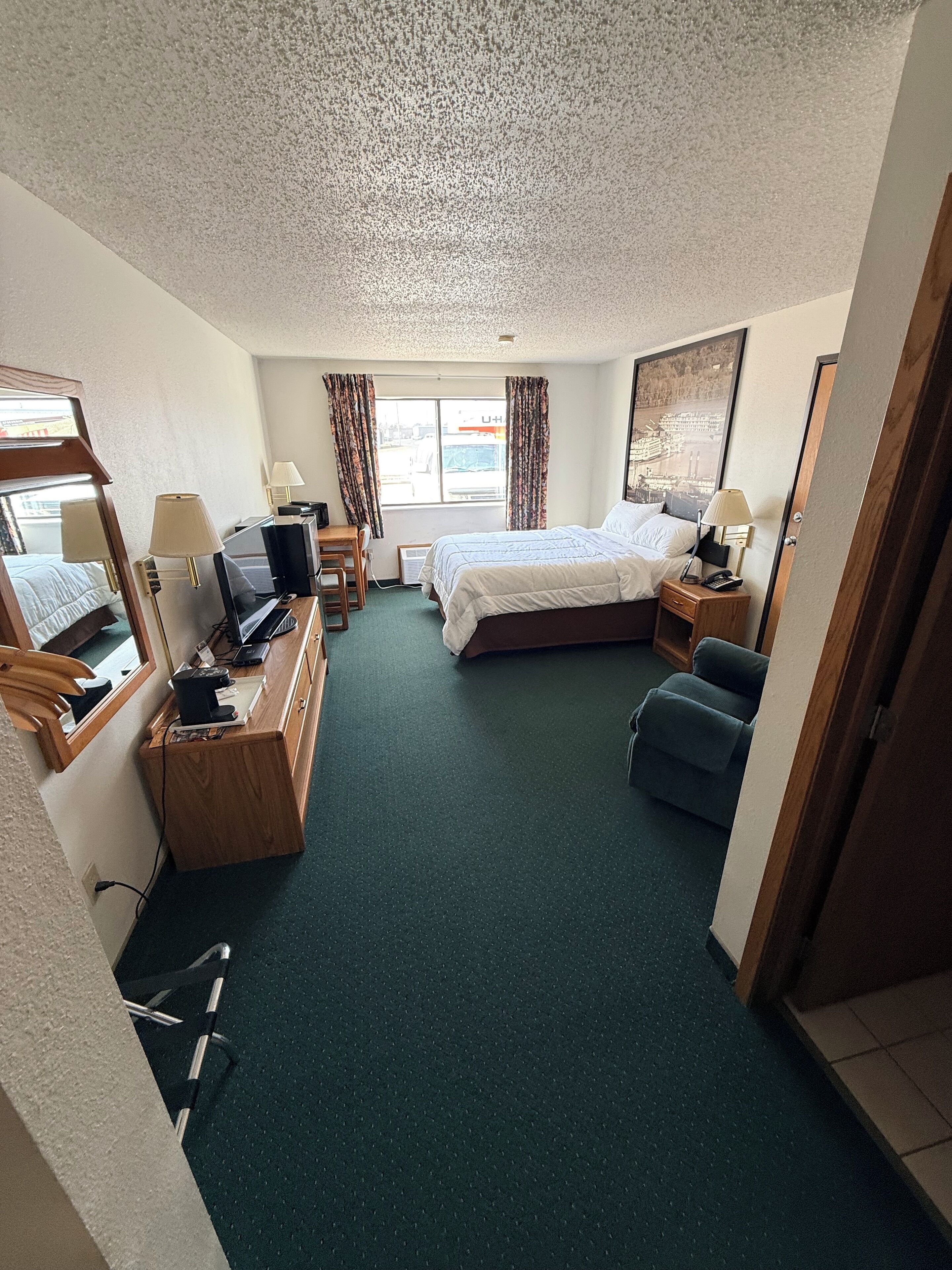 A hotel room with a bed, desk, chair, and a view of the outside.