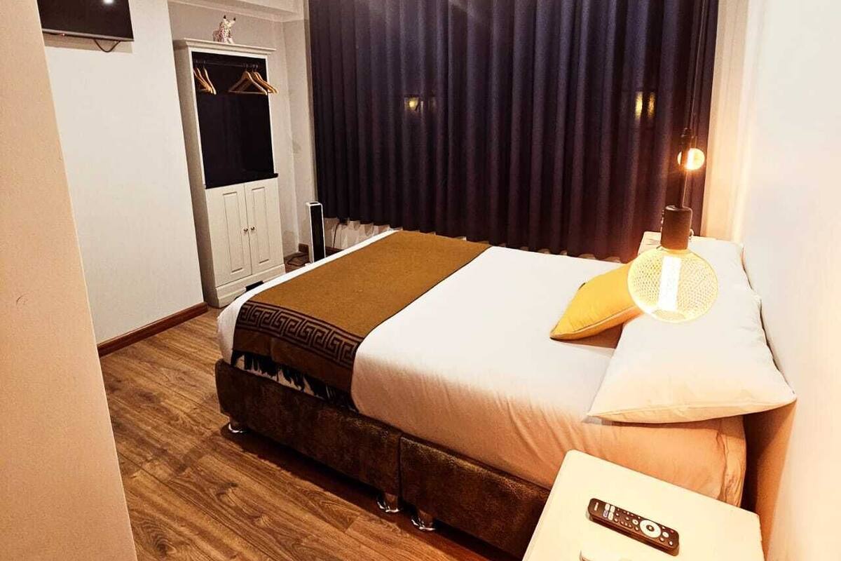 A hotel room with a bed, a bedside table with a lamp, a TV mounted on the wall, and a wardrobe.