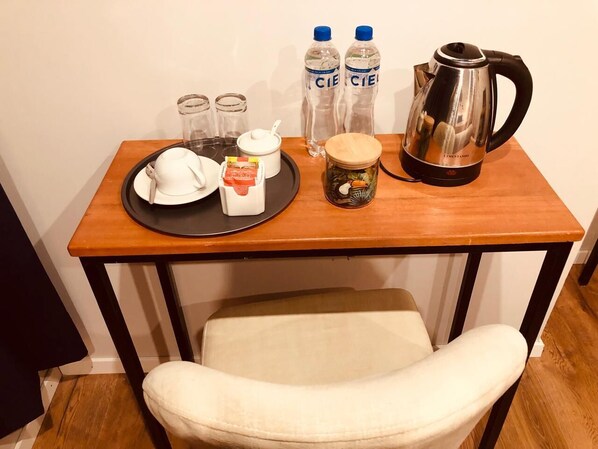 Una pequeña mesa con una taza de café, una tetera, dos botellas de agua, un tarro de té y un plato con una bolsita de té y un sobre de azúcar.