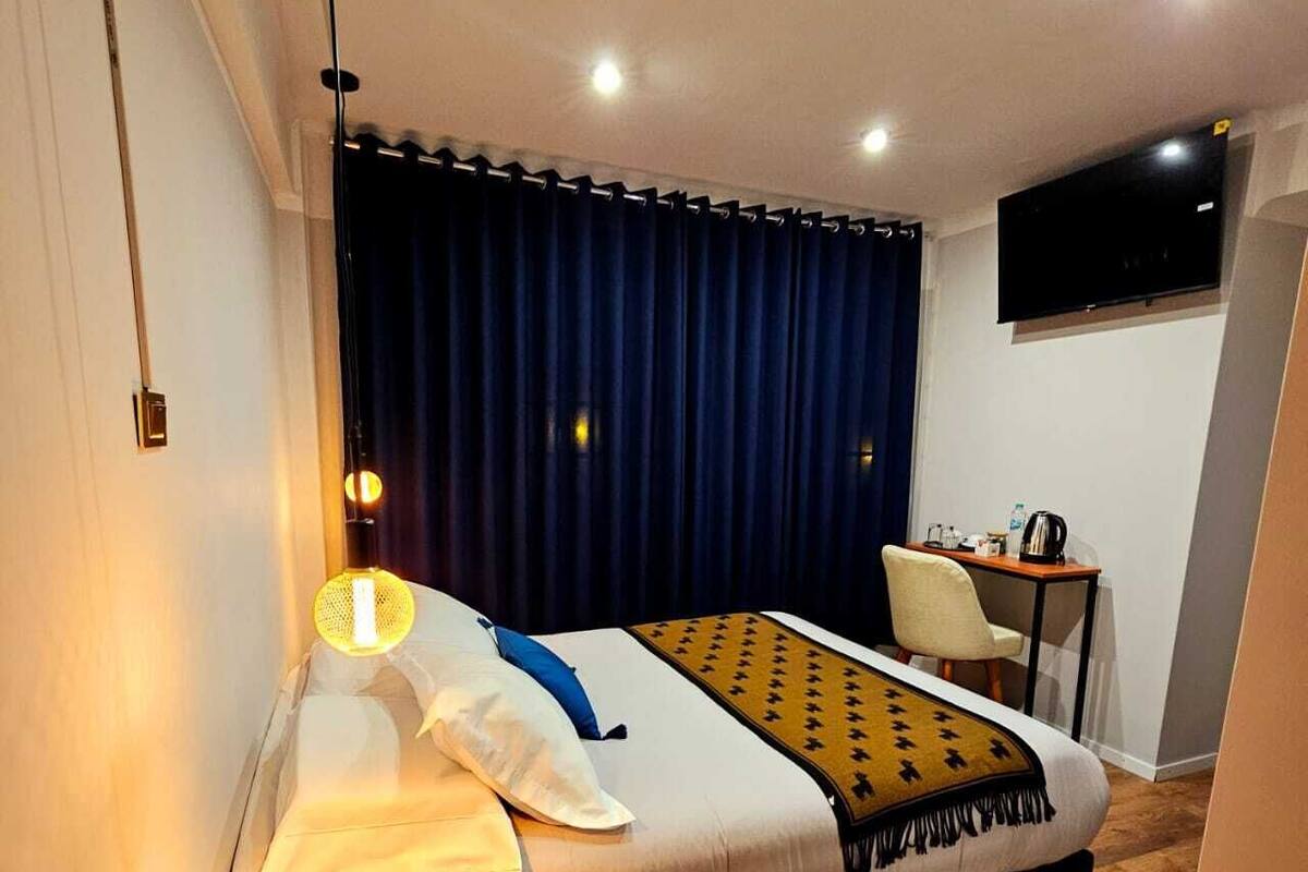 A hotel room with a bed, a desk, a chair, a TV, and a lamp.