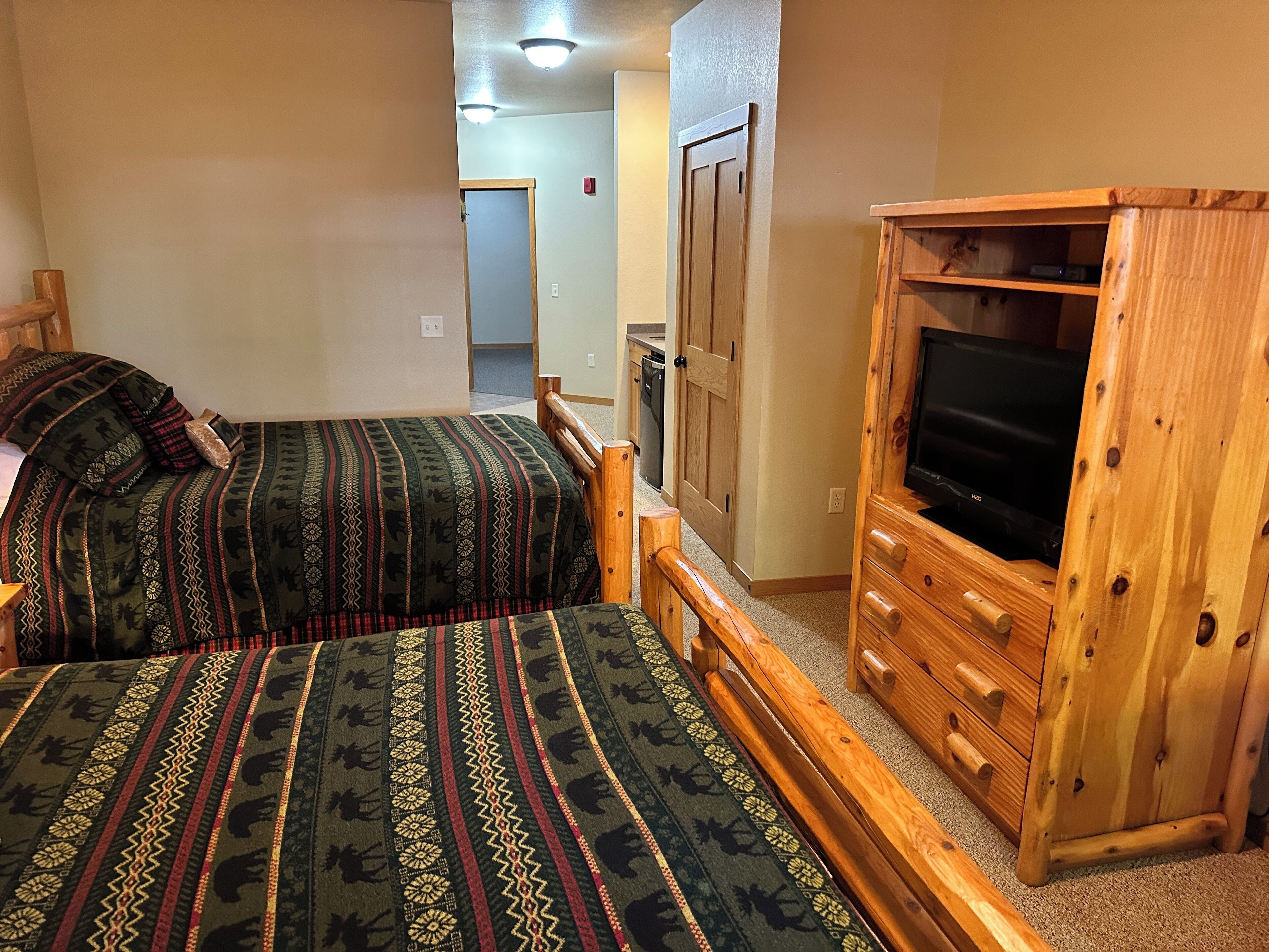 Une chambre avec deux lits, un meuble en bois pour la télévision et une porte donnant sur une autre pièce.