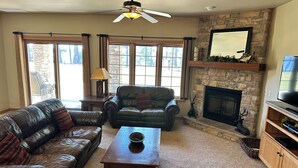 A living room with a stone fireplace, leather sofas, a wooden coffee table, and a television on a wooden stand. - Spirit of the Northwoods (eagle river)