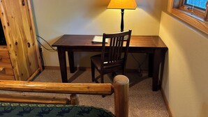 A wooden desk with a lamp, a chair, and a window with a view of trees. - Studio 111 By Eagle Waters Resort (eagle river)