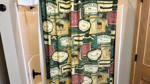 A bathroom with a shower curtain featuring a forest and moose design, a white bathtub, and a wooden door. - Studio 111 By Eagle Waters Resort (eagle river)