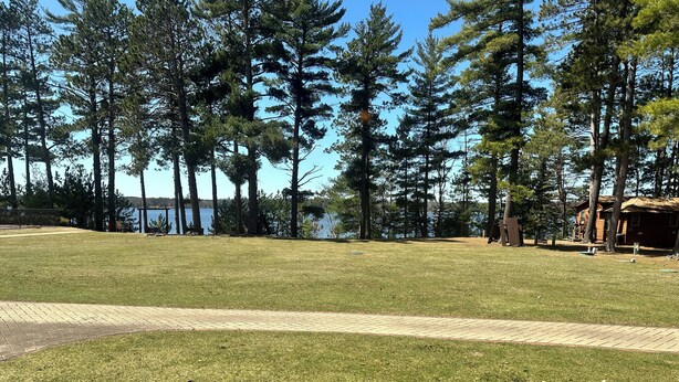A grassy area with a paved path, surrounded by tall trees and a body of water in the background. - Studio 112 By Eagle Waters Resort (eagle river)