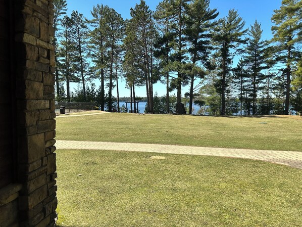 A grassy area with a stone wall, a paved path, and tall trees.