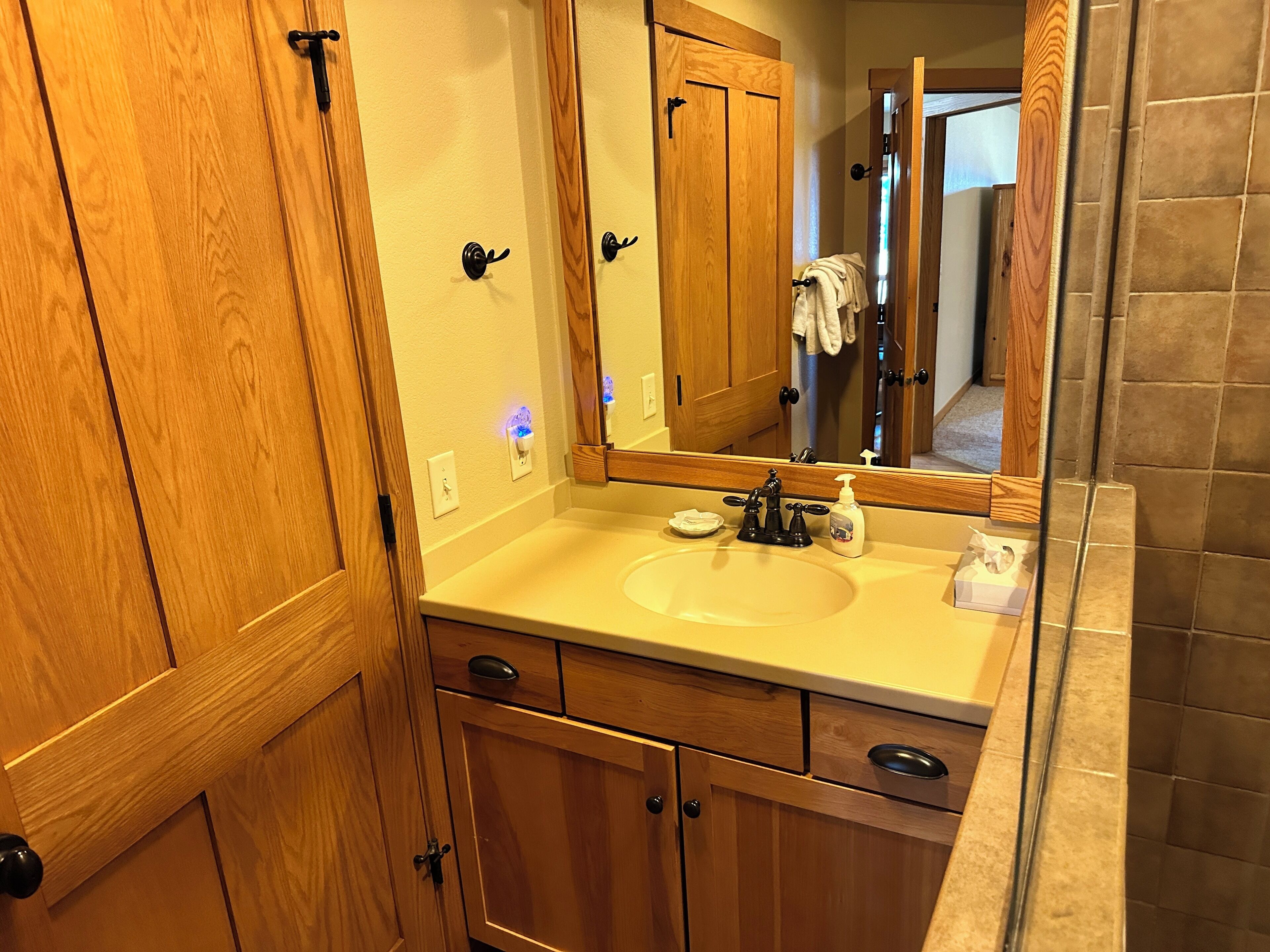 Une salle de bain avec des meubles de rangement en bois, un lavabo, un miroir et un porte-serviettes.