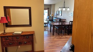 Un escritorio de madera con cajones y una lámpara, un espejo, y una zona de comedor con sillas y una mesa.