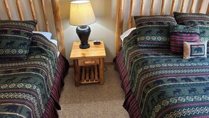 A room with two wooden beds, each with patterned bedding and pillows, a small wooden nightstand with a lamp, and a wall clock. - Studio 113 By Eagle Waters Resort (eagle river)