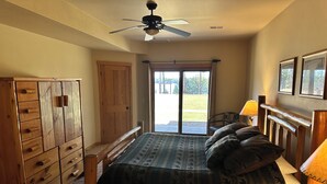 A bedroom with a bed, wooden dresser, ceiling fan, and a view of the outdoors. - CONDO 103 by Eagle Waters Resort (eagle river)