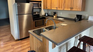A modern kitchen with wooden cabinets, stainless steel appliances, a granite countertop, and a built-in sink. - CONDO 105 by Eagle Waters Resort (eagle river)